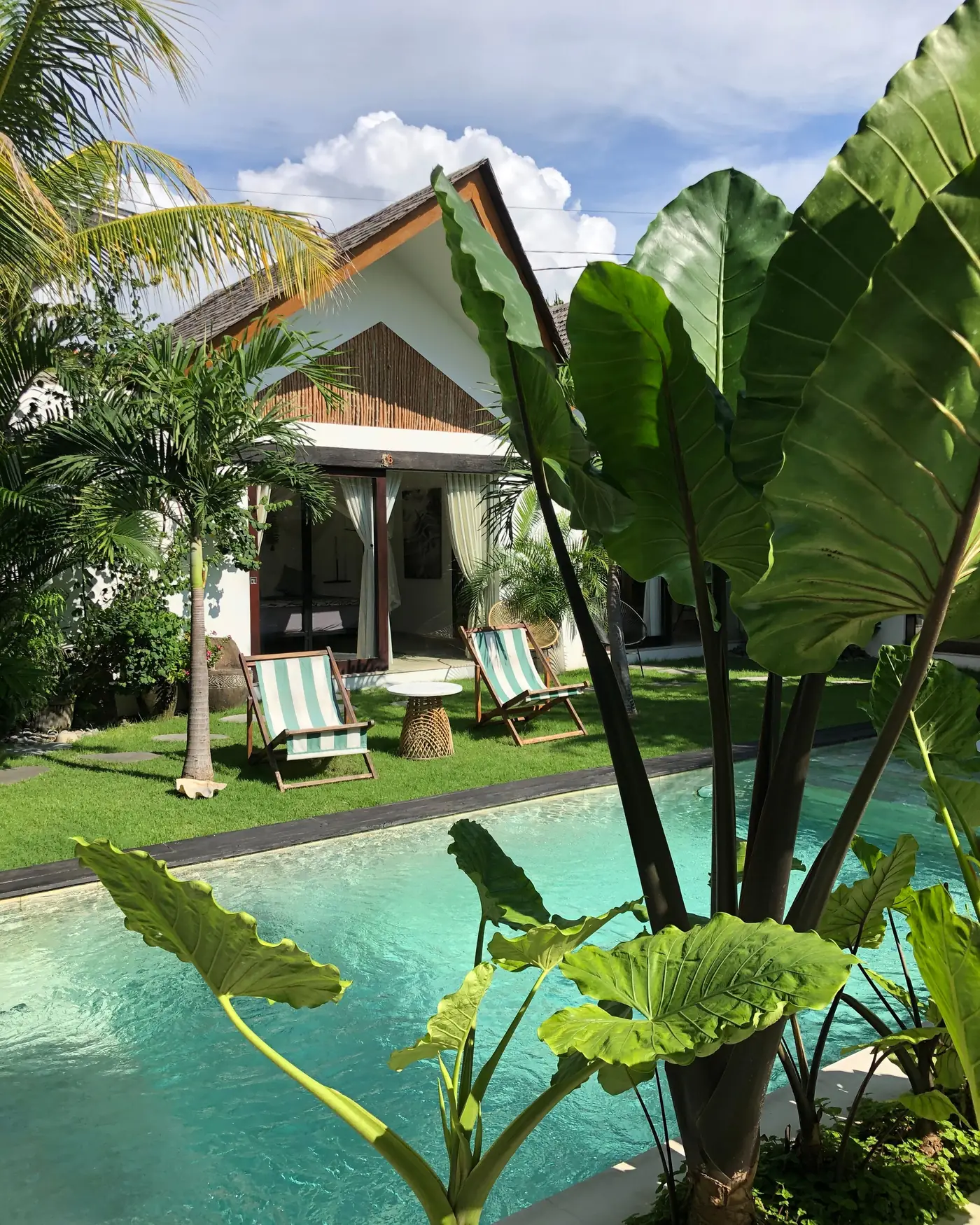 A small Balinese guesthouse with a pool and two deckchairs on the lawn