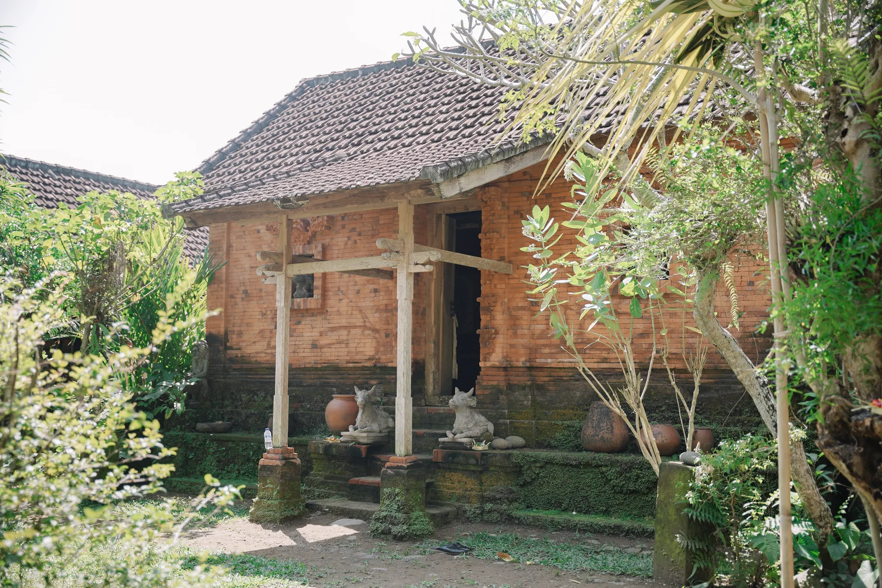 A traditional red-brick Balinese pavilion with a tiled roof, surrounded by garden greenery at Omah Blumbungan