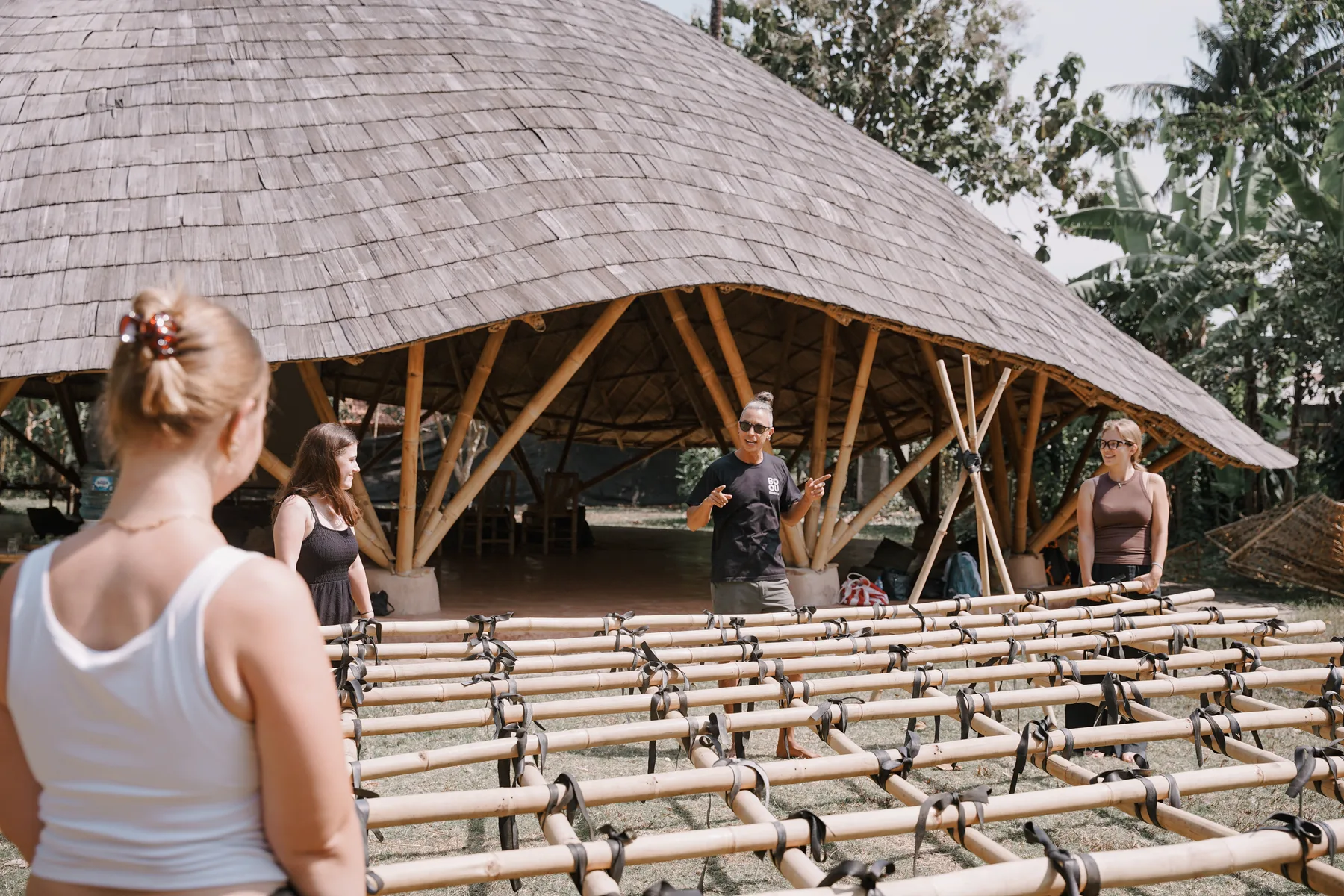 An instructor talking to students in front of a bamboo pavilion at BambooU, with a lashed bamboo frame in the foreground