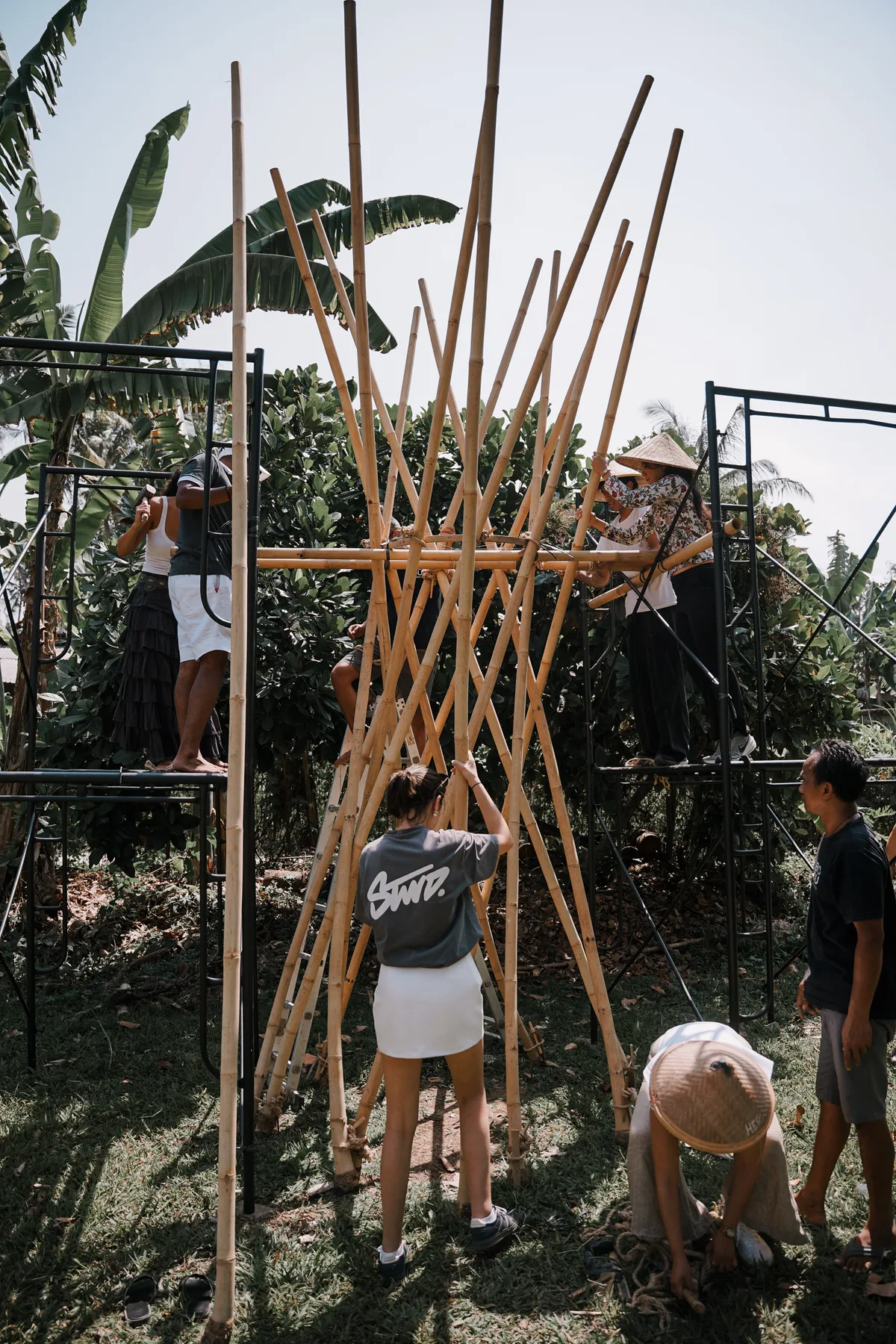 Students on scaffolding lashing tall bamboo poles into a conical structure at BambooU
