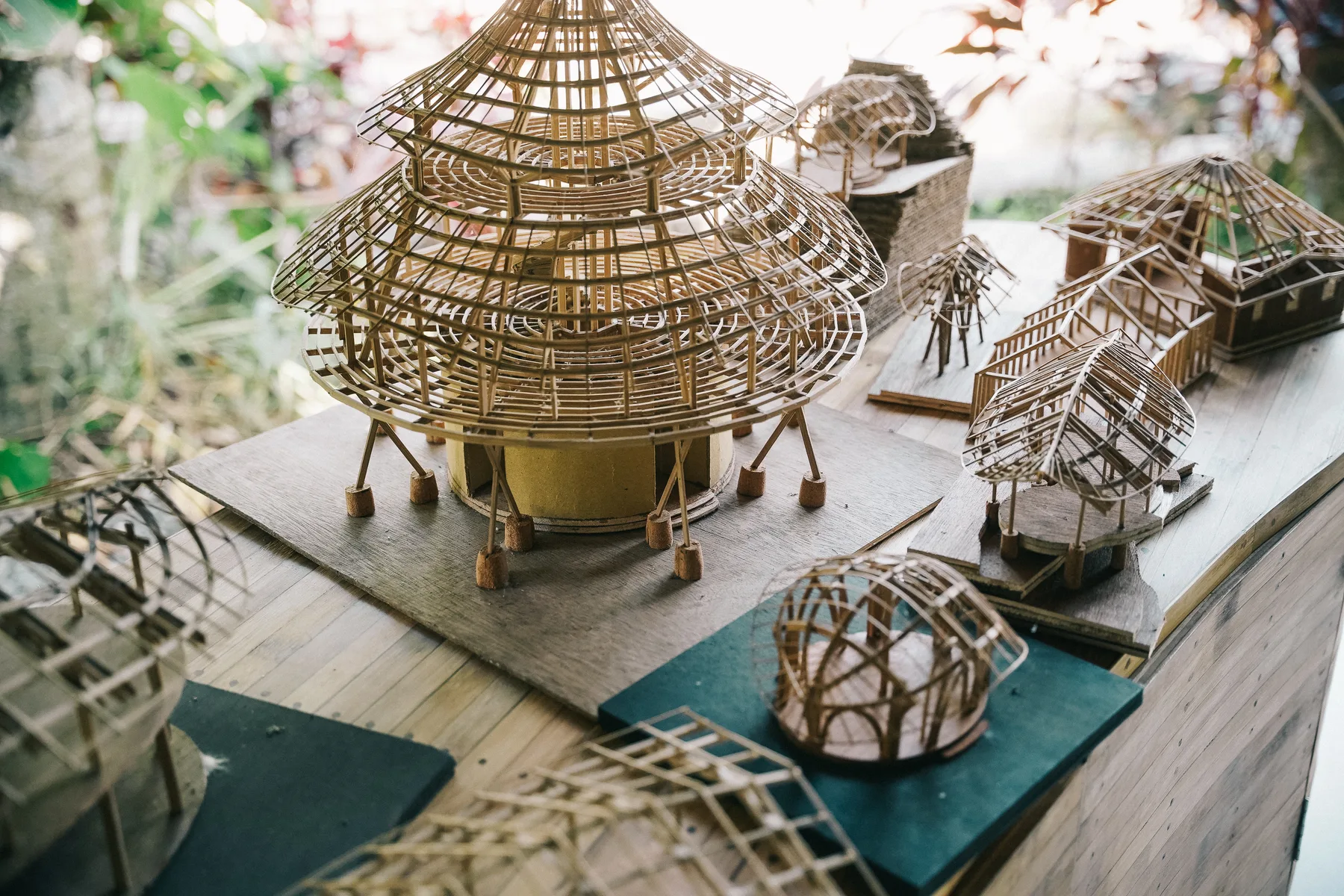 Detailed bamboo architecture models on a workshop table, showing roof structures at different stages of completion
