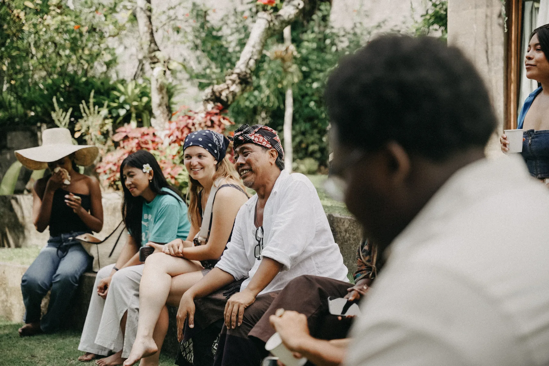 A group of students and a local guide sitting together in a garden at Titi Ubud, listening and smiling