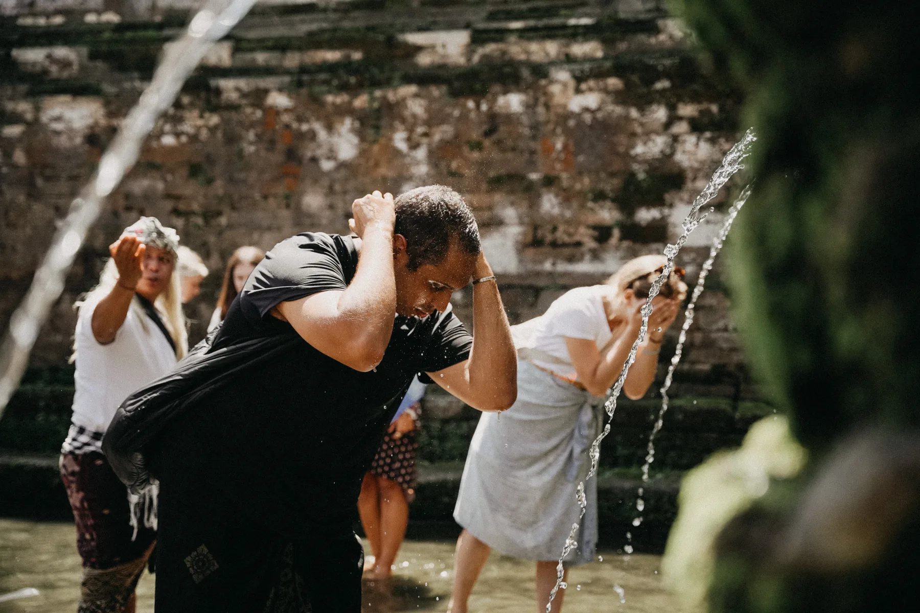 Students washing at a holy spring, water streaming from carved stone spouts at Goa Gajah