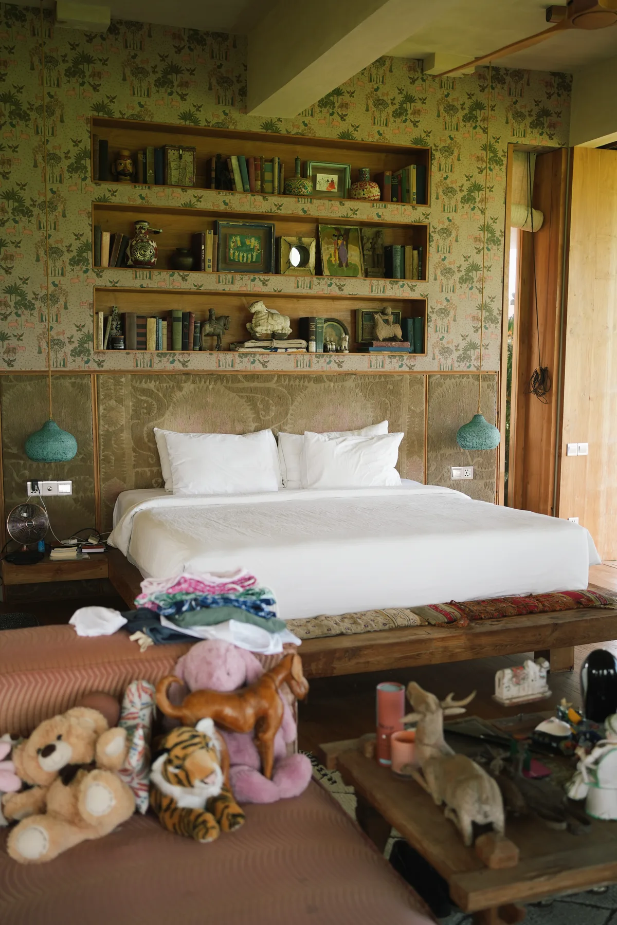 A guest bedroom at Villa Nenek with patterned wallpaper, built-in shelves of books and objects, and a large white bed