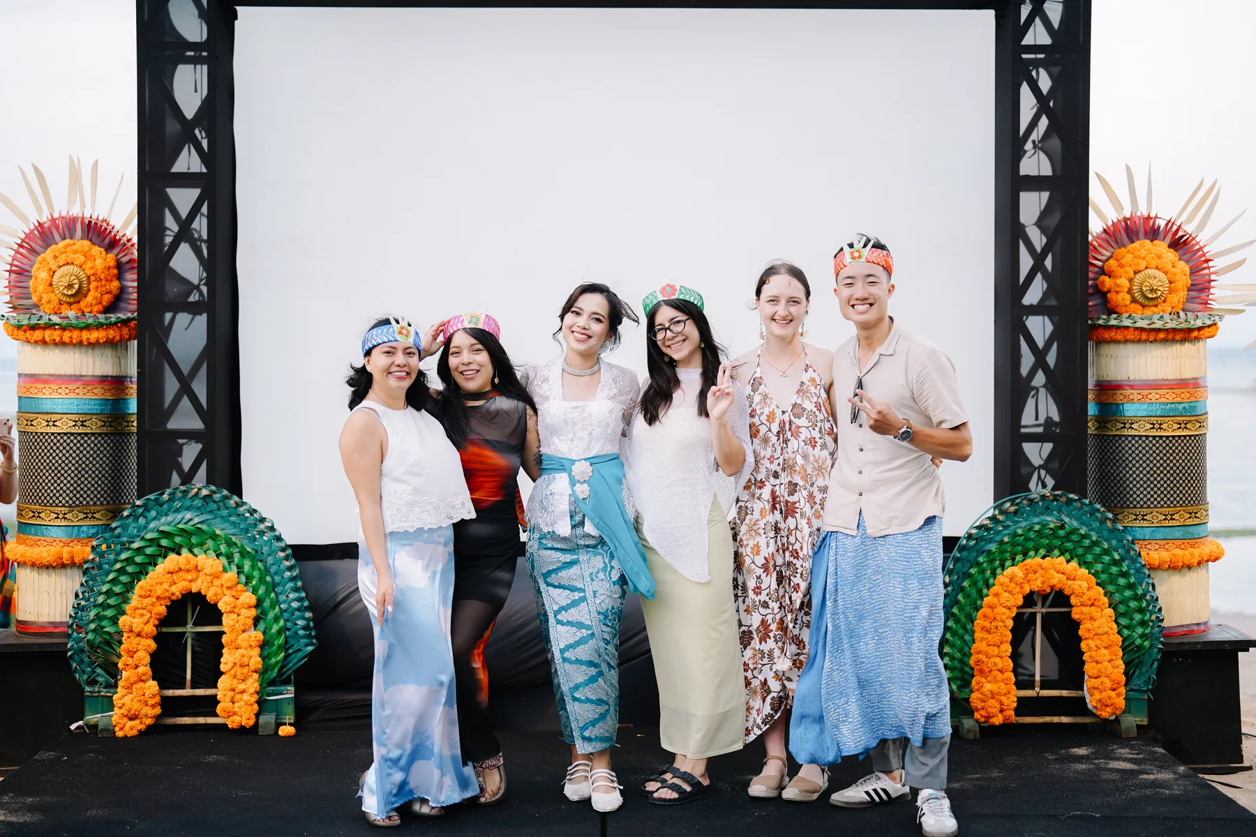 A group of students posing on a decorated stage with traditional Balinese headpieces at the Farewell Closing Ceremony