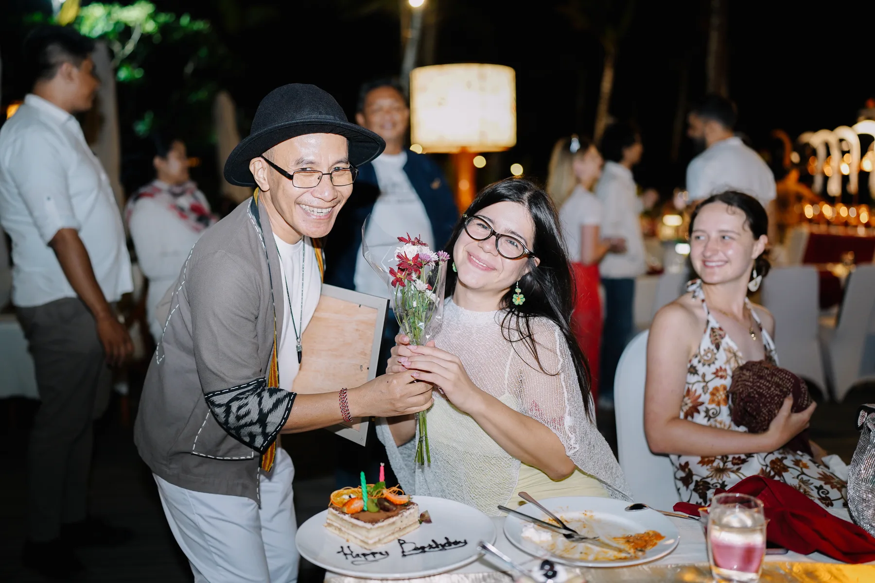 Students smiling around a table with a cake reading Happy Birthday and a small bouquet of flowers at the closing dinner