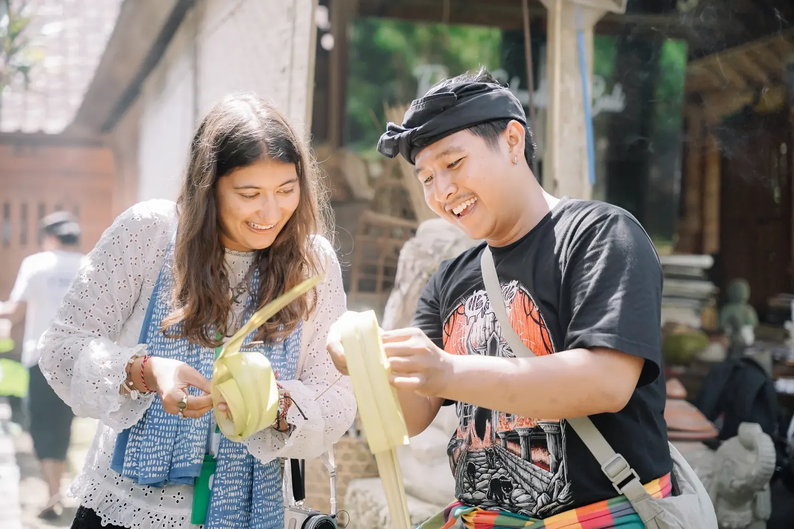 A student and a Balinese guide folding palm-leaf offerings together at Omah Blumbungan, both smiling