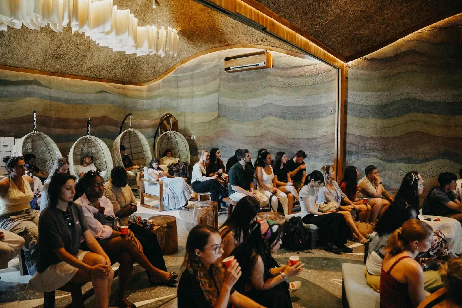 Students seated in a rammed-earth amphitheater lounge with hanging pod chairs at Nuanu