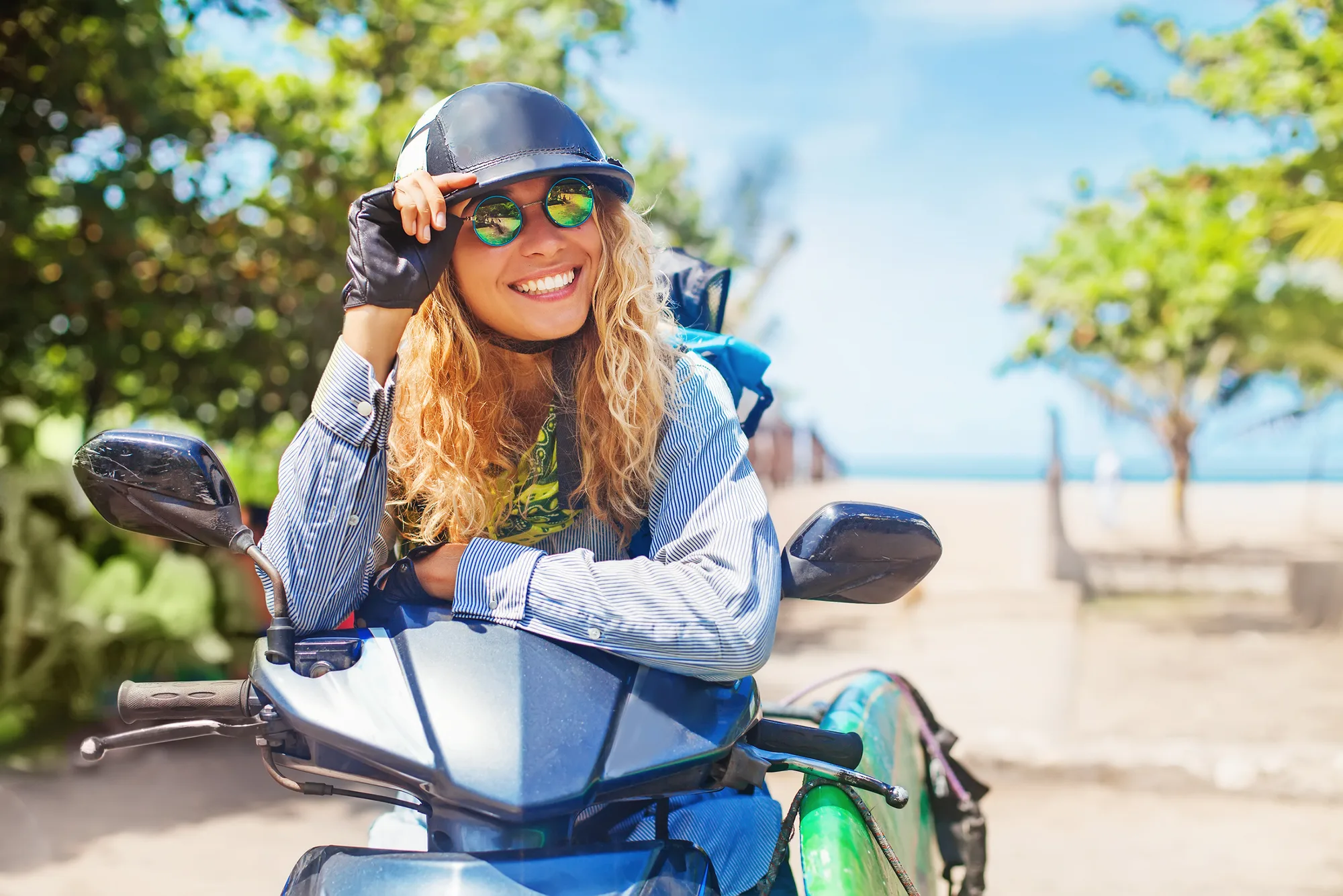 A young woman leaning on the handlebars of a parked scooter by the coast