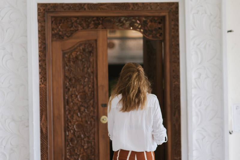A StudyInBali student entering a classroom at Universitas Udayana (UNUD) through a wooden door, ready for a study abroad session.